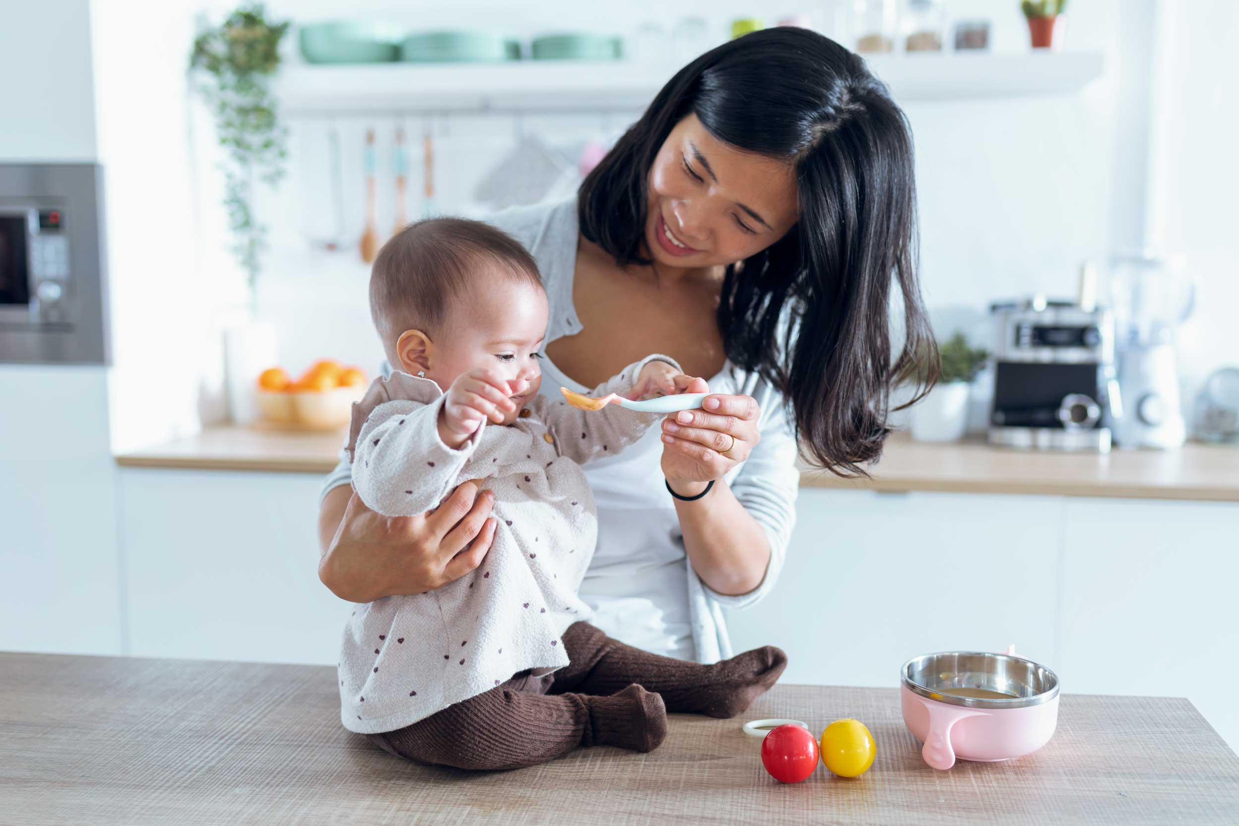 happy-young-mother-feeding-her-cute-baby-girl-with-2022-02-02-04-50-22-utc.jpg